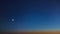 Aerial panoramic time lapse of the crescent moon and star descending towards the horizon in a dark blue sky in the twilight after