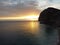 Aerial panoramic view of beautiful sunset above calm azure sea and volcanic rocky shores. Sun glare, small waves on the