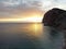 Aerial panoramic view of beautiful sunset above calm azure sea and volcanic rocky shores. Sun glare, small waves on the