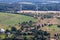 aerial panoramic view of green village with houses, barns and gravel road in forest with windmills