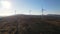 Aerial panoramic view of a group of wind turbines with rotating blades working on a hill with a background of mountains