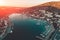 Aerial panoramic view of harbor of small mountain town with yachts and boats in bay, sea coast and resort at sunset