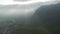 Aerial panoramic view of hazy landscape against sun shining through clouds. Forwards fly along high steep slope. Iceland