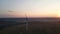 Aerial panoramic view of rotating blades of wind turbine against scenic sunset, the sun goes down over horizon