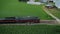 Aerial Parallel View of an Antique Steam Passenger Train Blowing Smoke Passing Families and Children Watching as it Travels Thru P