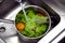 Aerial photo of an inox saucepan with vegetables washing under a tap