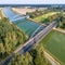 Aerial photograph of infrastructural facilities for cars, trains and ships, overflight of a canal with a railway bridge and a road