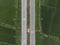 Aerial photograph of a yellow car running on a paved road that cuts through the green fields