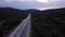 Aerial: road highway at sunset. Rides a lot of cars, headlights are included. Near mountains and forest.