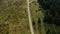 Aerial rocky woods road view among green spruce trees growing grassy hills