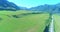 Aerial rural mountain road and meadow at sunny summer morning. Asphalt highway and river.