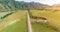 Aerial rural mountain road and meadow at sunny summer morning. Asphalt highway and river.