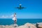 Aerial Serenity: Girl in White Dress on Stones, Plane Soaring Above the Blue Sea