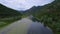 Aerial shooting river with green lilies on water surface flowing around hill.