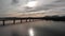 Aerial shot of a bridge crossing a reservoir while discovering mountains, with a sunset in the background