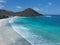 Aerial shot of the calm foamy waves of the ocean hitting the beach with hills in the background