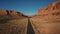 Aerial shot of car driving along straight American desert highway road among atmospheric rocky mountain canyon ridge.