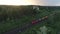 Aerial shot of cargo train running through the Church small village in the woods at sunset