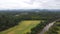 Aerial shot of countryside with green field surrounded by lush dense forests next to narrow river