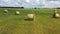 Aerial shot flying around hay rolls in green meadow. Cloudy sky background