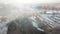 Aerial shot flying towards Venta river waterfall and long brick bridge in foggy winter morning, Kuldiga, Latvia.