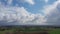 Aerial shot flying towards white clouds and green lush farmland fields