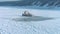 Aerial shot of frozen ship or tugboat staying on river covered with ice in winter at background of snow forest