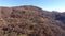 Aerial shot, little village in the middle of an autumn wood in the mountains with orange dry leaves, sun high in the sky, filmed w