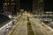 .aerial shot of a long street at night with tall light posts along the sidewalk with bare winter trees, skyscrapers