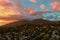 Aerial shot of majestic mountains with powerful clouds and blue sky with homes, apartments and lush green trees at sunset