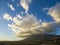 Aerial shot of majestic mountains with powerful clouds and blue sky with homes, apartments and lush green trees at sunset