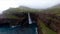 Aerial shot of Mulafossur waterfall and a cliffed coast in Vagar, Faroe Islands