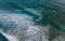 Aerial shot over blue coral reef bay wide waves with kiteboarder riding orange power kite. Active sport people and beauty in