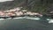 Aerial shot. Panorama of a small town at the base of the mountain. Volcanic shore of the ocean. Waves beat on the