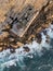 Aerial shot of a ruined rugged wall with rock pieces fallen on a wavy coast in Peniche, Portugal