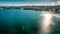 Aerial shot of a sea reflecting sunshine with a cityscape in the background