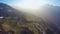 Aerial shot of small farming village on green hill of mountain in rays of sunset