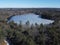 Aerial shot of a small frozen lake surrounded by pine trees in the daylight