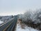 Aerial shot of trees, highway and field covered with snow on a cold winter day