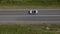 Aerial shot of a white convertible driving down an empty country road.