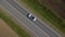 Aerial shot of a white convertible driving down an empty country road.