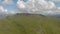 An aerial sideway right to left footage of a rocky summit mountain with green slope and trail path under a majestic blue sky