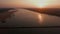 Aerial silder shot of vehicles crossing a bamboo bridge over a river at orange sunset