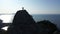 Aerial silhouette of a young loving couple standing on the top of a mountain over the sea at sunrise and waving hands