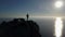Aerial silhouette of young woman standing on the top of a mountain facing the sea. Lady on the summit in beautiful