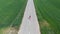 Aerial slow motion: drone tracking man running alone on countryside road crossing cultivated fields, outdoor activities fitness we