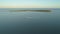 AERIAL: Small fishing boat leaves a trail in blue ocean water as it passes islet