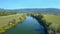 AERIAL Spectacular shot of dark blue stream and vast green farmlands in Slovenia