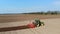 Aerial survey, large tractor with special equipment rides through plowed field of black soil, forms even rows for