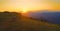 AERIAL: Three mountain bikers speeding down a grassy hill at golden sunset.